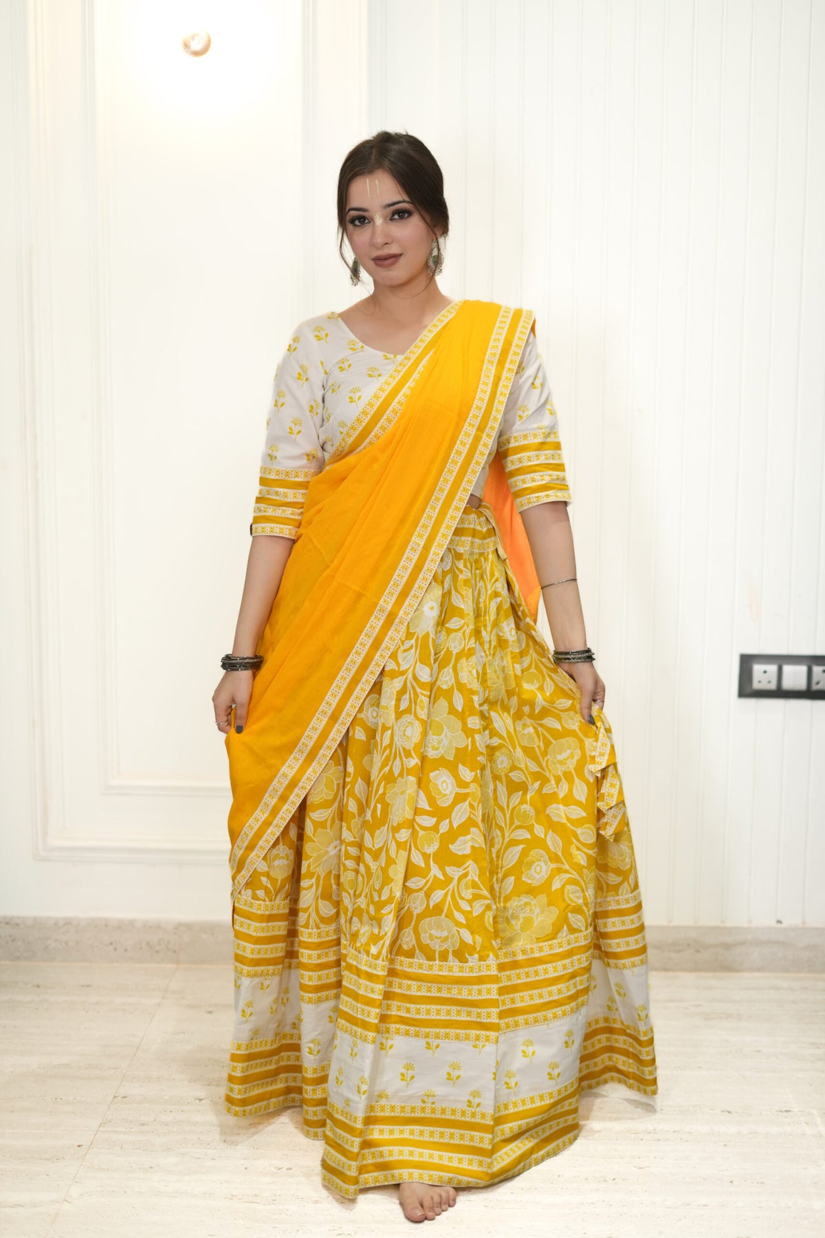 Woman wearing a yellow saree with a white blouse in a room.